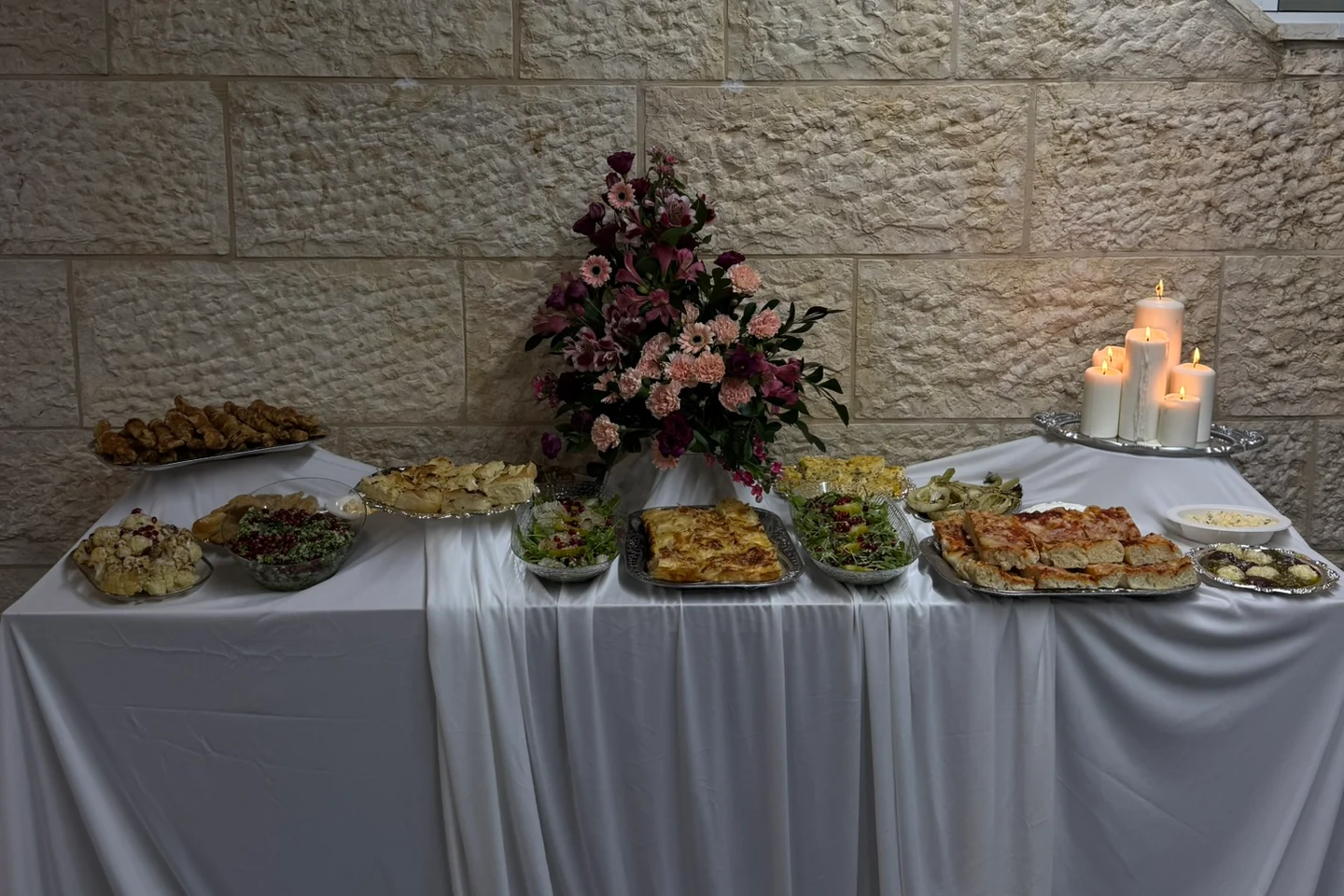 מבט חזיתי על שולחן בבד לבן עם פרחים, נרות ומגשי הגשה